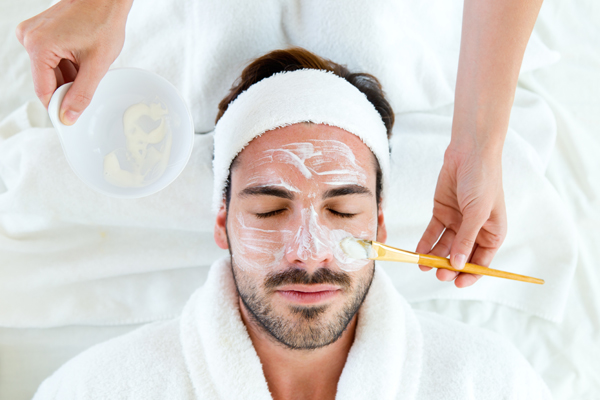 Portrait of man with clay facial mask in beauty spa.